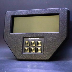 May include: A black Stream Deck device with a rectangular screen and six illuminated buttons. The device has a textured surface and the Stream Deck logo is visible. The screen is dark, and the buttons are gold.