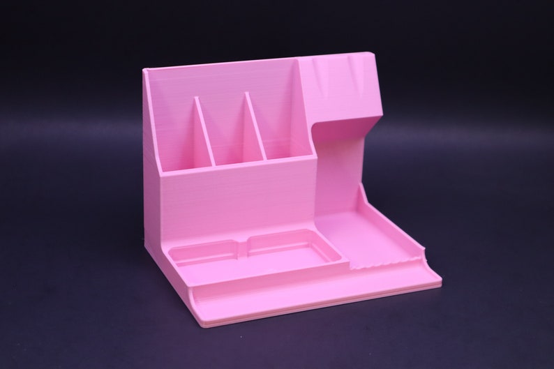 May include: A pink plastic desk organizer with four compartments, a small tray, and a larger tray. The organizer is designed to hold pens, pencils, and other office supplies.