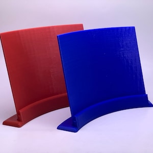 May include: Two 3D printed display stands, one red and one blue, with a curved base and a flat rectangular surface.