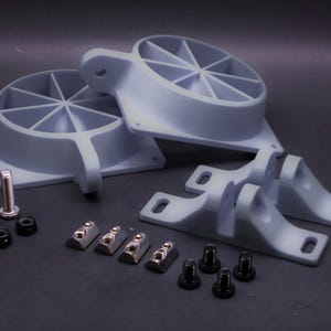 Może przedstawiać: Zestaw jasnoszarych komponentów mechanicznych, w tym dwie części w kształcie wachlarza, wsporniki, śruby i nakrętki. Części ułożone są na ciemnej powierzchni, sugerując zestaw do montażu lub naprawy.