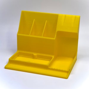 May include: A yellow plastic desk organizer with multiple compartments for pens, pencils, and other office supplies. The organizer has a large tray on the bottom for holding larger items.