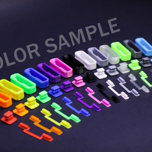 May include: A collection of colorful plastic components, including rectangular frames, square buttons, and elongated levers, arranged on a dark surface. The components are in various colors such as red, orange, yellow, green, blue, purple, black, and white. The text "COLOR SAMPLE" is visible.