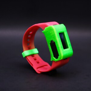Pode incluir: Uma pulseira vermelha e verde com um visor digital. A pulseira &eacute; feita de silicone e tem uma capa de pl&aacute;stico verde sobre o visor.