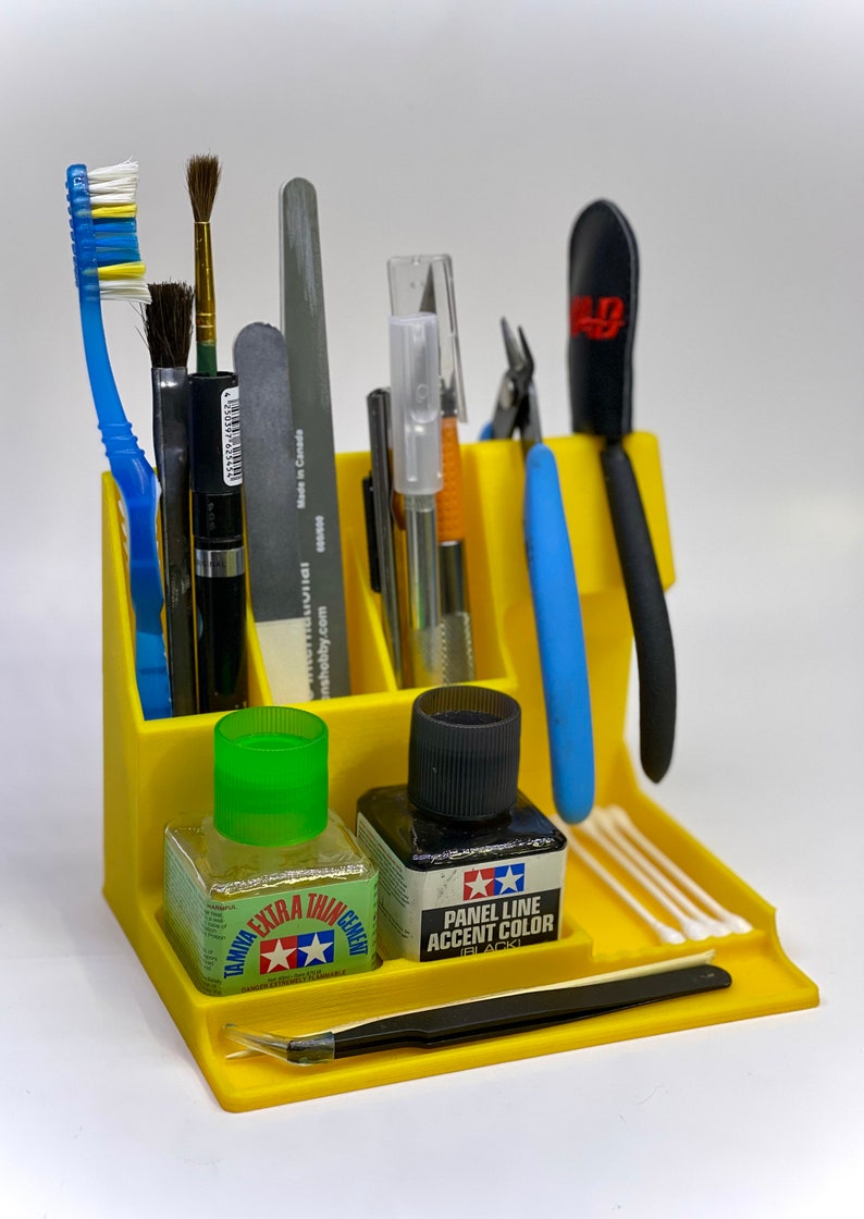 May include: Yellow plastic organizer with compartments for tools and supplies. It includes a pair of tweezers, two bottles of paint, a pair of pliers, a pair of scissors, a brush, a file, and cotton swabs.