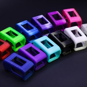 Pode incluir: Um conjunto de 12 capas coloridas impressas em 3D para um rastreador de fitness. As capas est&atilde;o dispostas em uma linha, com cores que variam do vermelho ao roxo.