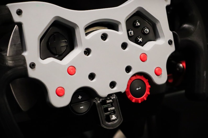 May include: Close-up of a gray racing wheel with red buttons and a black knob. The wheel has a PlayStation logo and buttons labeled "Mode", "Option", and "Share".