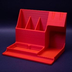 May include: A red plastic desk organizer with multiple compartments for pens, pencils, and other office supplies. The organizer has a raised section for a phone or other small items.