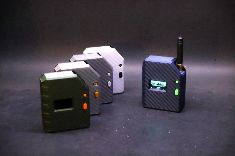 May include: A collection of small, rectangular electronic devices with a carbon fiber texture. The devices are in various colors, including green, gray, and blue. One device has a small screen and antenna.
