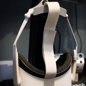 May include: White virtual reality headset with a black headband and white straps hanging from a hook.