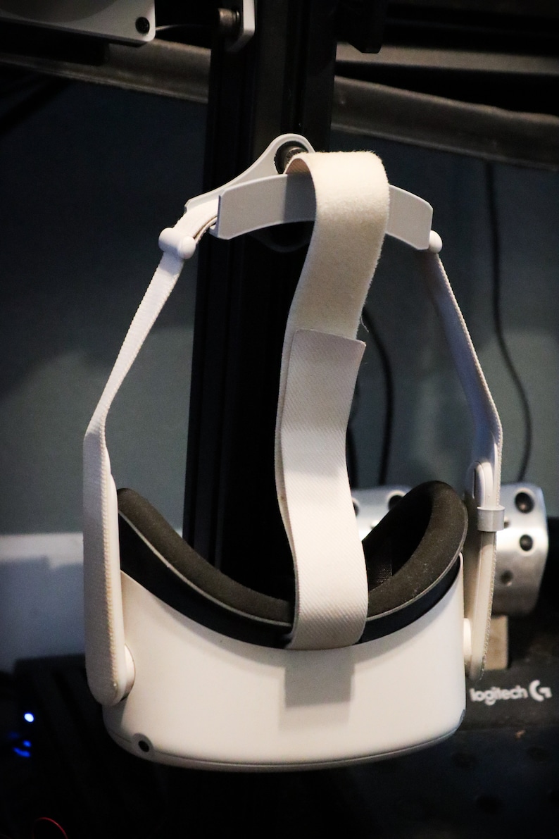 May include: White virtual reality headset with a black headband and white straps hanging from a hook.