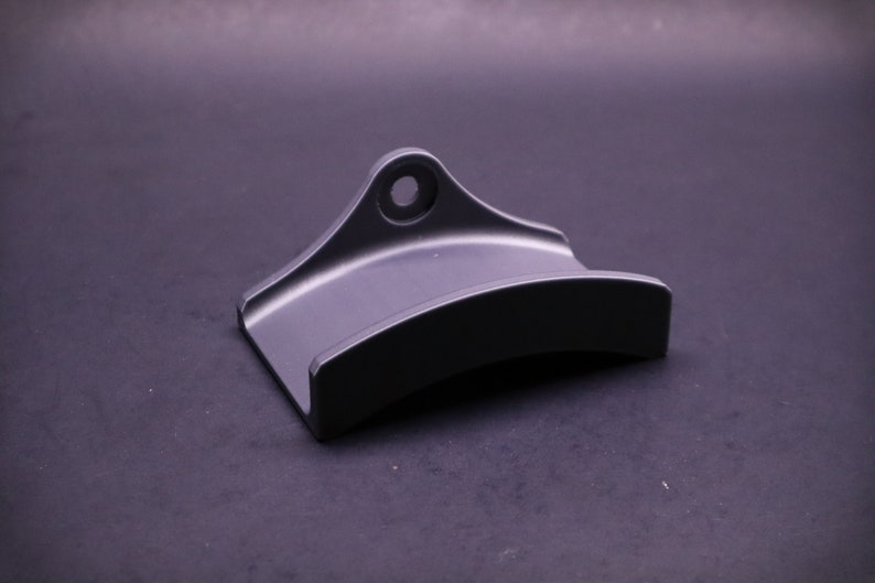 May include: A black metal wall mount with a curved shape and a hole for hanging.