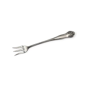 May include: A silver-colored fork with three tines. The handle is long and slender, with a decorative floral design at the end. The edges of the handle are lined with small, raised dots. The fork is set against a white background.