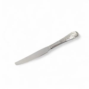 May include: A single silver butter knife with a decorative handle featuring floral and grape cluster engravings. The knife has a long, slender blade and is set against a white background. The handle is slightly curved.