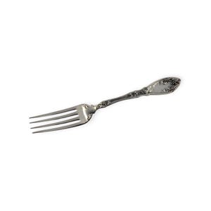 May include: A silver fork with four tines and a decorative handle. The handle features an embossed floral and grape design. The fork is made of a shiny, metallic material and is set against a white background. This vintage fork is suitable for formal dining.