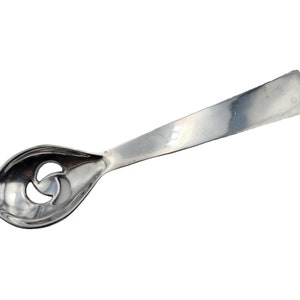 May include: A silver-colored spoon with a unique design. The spoon's bowl features a decorative, three-part cutout. The handle is flat and rectangular. The spoon is likely made of stainless steel or a similar metal.