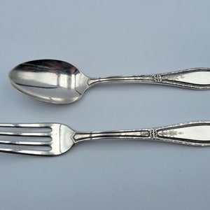 May include: A silver fork and spoon set with ornate handles. The utensils are laid out on a white background.
