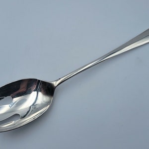 May include: A silver serving fork with a long handle and a wide, oval-shaped head with three prongs.