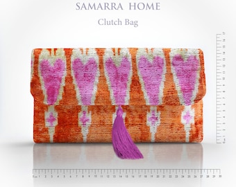 May include: An orange clutch bag with a pink heart-shaped pattern and a purple tassel. The bag is approximately 12 inches long. Text on the image reads "SAMARRA HOME" and "Clutch Bag".
