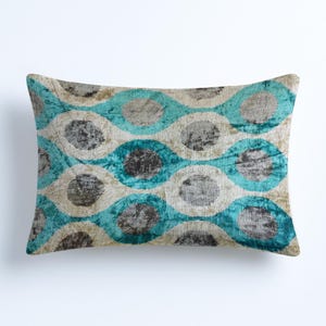 May include: Rectangular decorative pillow with a repeating pattern of teal, gray, and beige circles. The pillow has a soft, textured appearance, suggesting a velvet or similar fabric. The design is symmetrical and modern.