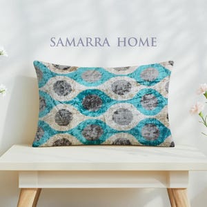 May include: Rectangular decorative pillow with a teal, gray, and cream geometric pattern. The pillow is on a white table. The text "SAMARRA HOME" is above the pillow.