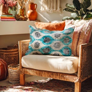 May include: A wicker armchair with a cream-colored cushion holds a decorative pillow with a teal, gray, and white circular pattern. Other pillows in shades of orange and pink are visible. The room is decorated with baskets, plants, and a rug.