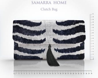 Puede incluir: Bolso de mano rectangular con un estampado de rayas de cebra en blanco y negro. El bolso tiene un cierre de solapa y una borla negra. El texto "SAMARRA HOME" y "Clutch Bag" están impresos en la parte superior. Mide unos 30 cm de largo.