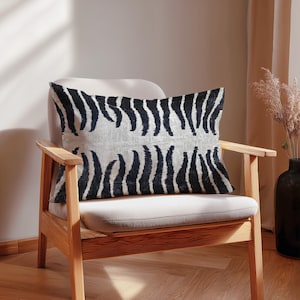 May include: A rectangular decorative pillow with a black and white zebra stripe pattern rests on a light-colored chair. The pillow's design features vertical black stripes against a white background. The chair has a wooden frame.