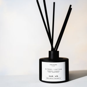 May include: Black diffuser bottle with black reeds. The label reads "Hand Poured No. 001 Citrus + Cotton Grapefruit + Mandarin Linen + Sandalwood wash + wik Small Batch // Orlando, FL"