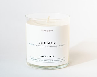 May include: A clear glass candle with a white label featuring the text "HAND POURED N° 020", "SUMMER", "BAMBOO • BERGAMOT • CEDARWOOD • COCONUT", "wash + wik", and "SMALL BATCH // SOY WAX CANDLE // ORLANDO, FL". The candle contains white wax and a single wick.