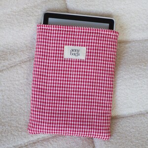 May include: Red and white gingham fabric e-reader case with the text "aeny bags" on a white label.