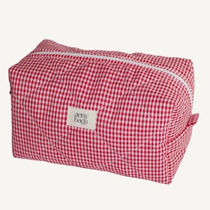 Könnte beinhalten: Rote und weiße karierter, gesteppte Kosmetiktasche mit einem weißen Etikett, auf dem "aeny bags" steht.