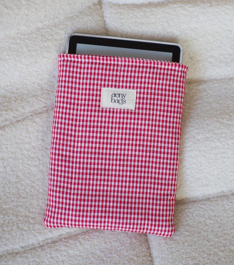 May include: Red and white gingham fabric e-reader case with the text "aeny bags" on a white label.
