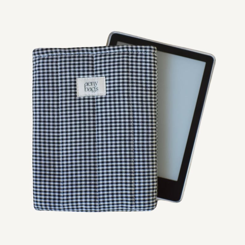 May include: Black and white gingham fabric e-reader case with a white label that says "aeny bags".