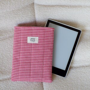 May include: Red and white gingham fabric e-reader case with a small white label that says "aery bags".