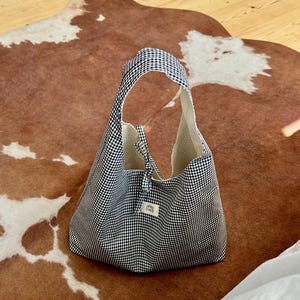 May include: A black and white gingham tote bag with a small white label that says "Petit Pan"