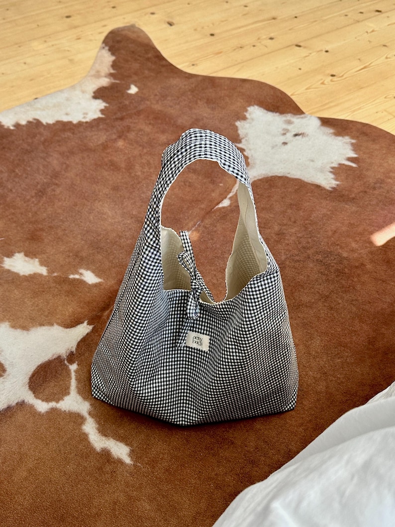 May include: A black and white gingham tote bag with a small white label that says "Petit Pan"