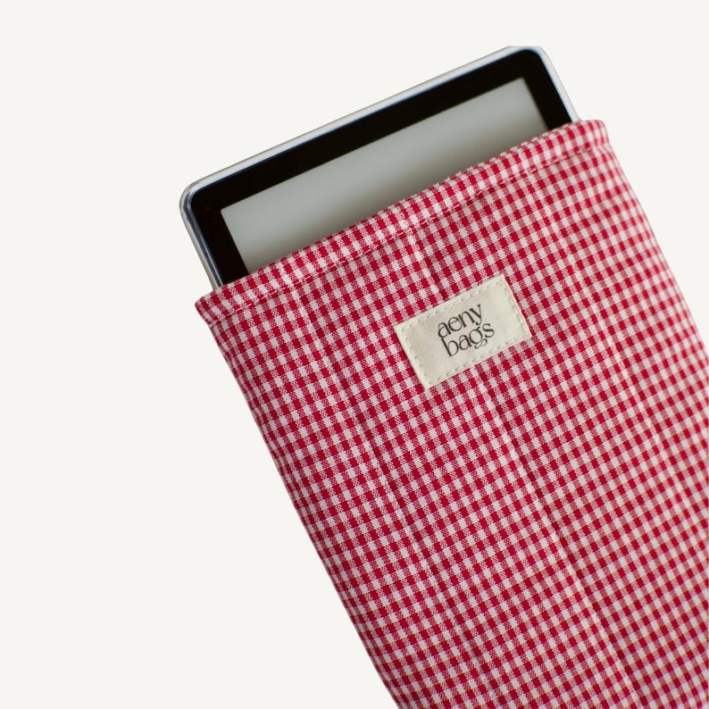 May include: Red and white gingham fabric e-reader case with a white label that says "aemy bags".