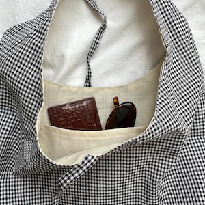 May include: A black and white gingham tote bag with a brown leather wallet and sunglasses inside.