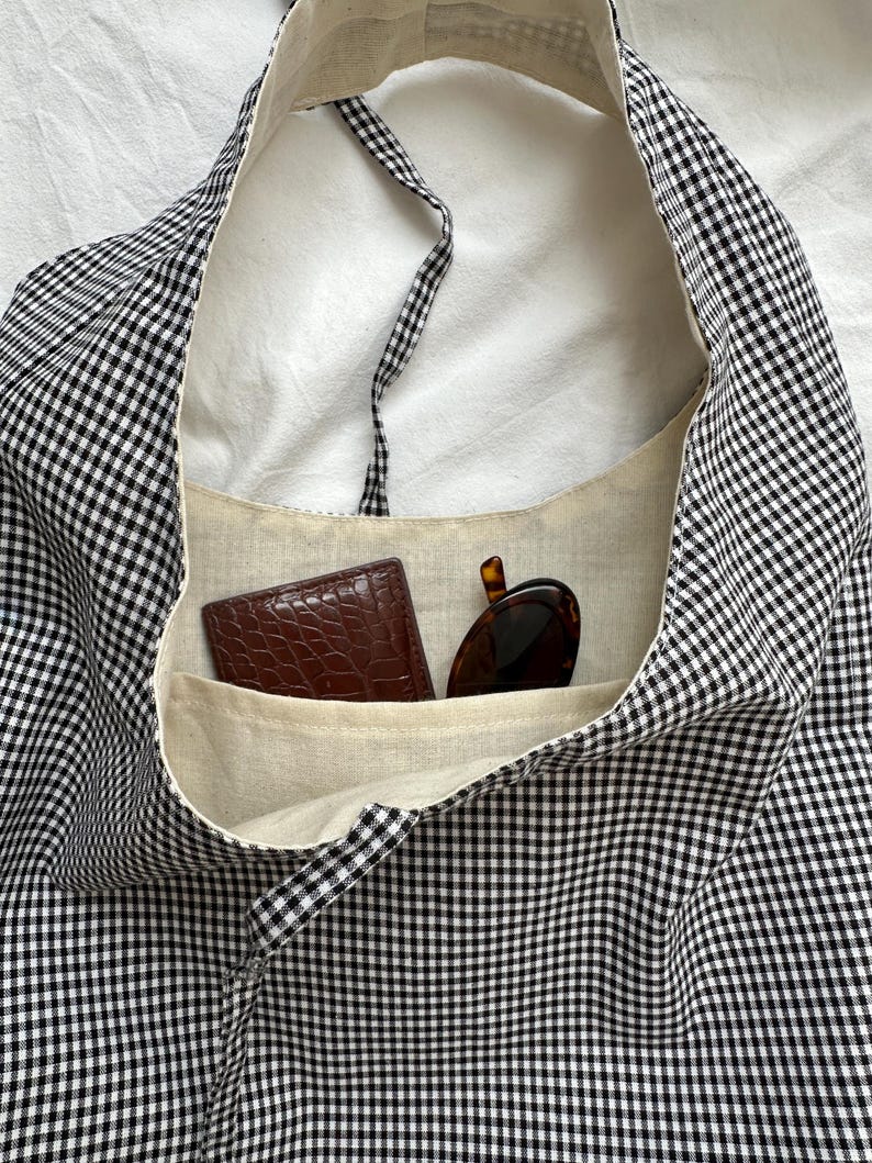 May include: A black and white gingham tote bag with a brown leather wallet and sunglasses inside.