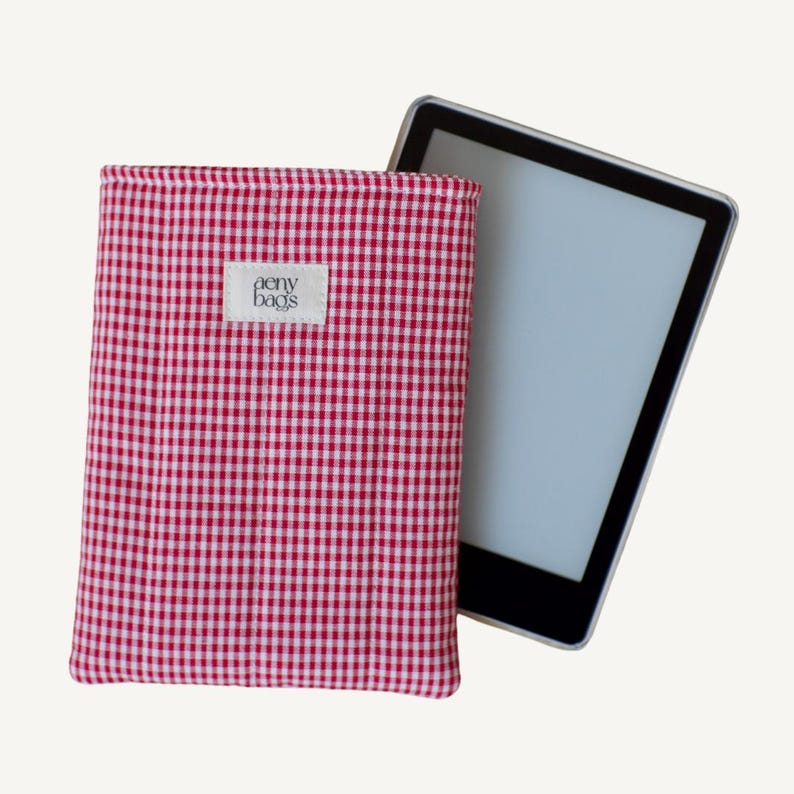 May include: Red and white gingham e-reader case with the text "aery bags" on a white label. The case is shown with an e-reader inside.