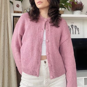 Könnte beinhalten: Ein rosa gestrickter Cardigan mit Knopfleiste und langen Ärmeln.