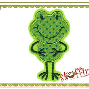 Könnte beinhalten: Grüne Frosch-Applikation mit blauen Punkten und einem lächelnden Gesicht. Der Frosch hat lange Arme und Beine und steht auf einem weißen Hintergrund.