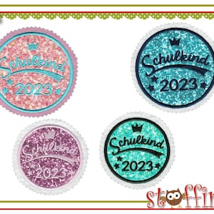 Könnte beinhalten: Vier runde, glitzernde, blaue, rosa und lilafarbene Patches mit weißem Rand. Jeder Patch hat eine Krone, den Text "Schulkind" und das Jahr "2023".