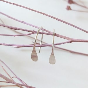 Könnte beinhalten: Ein Paar silberne Ohrringe in Tropfenform mit einem schlichten, minimalistischen Design. Die Ohrringe hängen an einem zarten Draht.