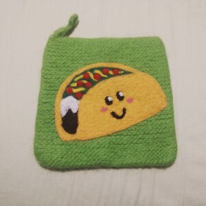 Może przedstawiać: Zielona dzianinowa torebka z uśmiechającą się żółtą aplikacją z filcu w kształcie taco. Taco ma czerwone i zielone dodatki i biały wir.