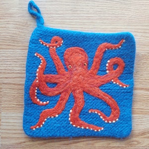 May include: A blue knitted pot holder with an orange octopus embroidered on it. The octopus has white eyes and white dots around its tentacles.