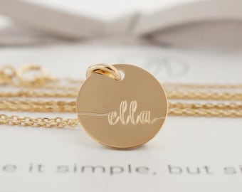May include: A gold-colored necklace with a round pendant engraved with the name "ella" in cursive script. The necklace is displayed on a white card with the text "Make it simple, but significant."