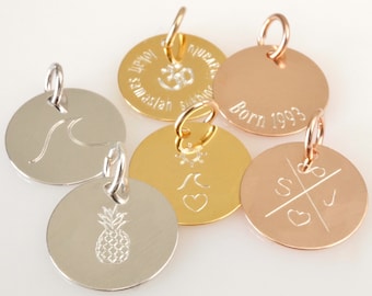 May include: A collection of round metal pendants in silver, gold, and rose gold. Each pendant features a unique engraved design, including a wave, pineapple, sun, heart, initials, and the text "Born 1993".