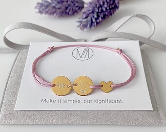May include: A pink string bracelet with three gold charms. The charms are round and have different engravings. The bracelet is on a white card with the text "Make it simple, but significant."