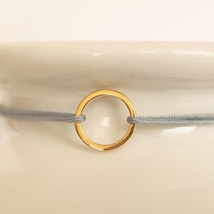 May include: A gold circle charm bracelet with a gray elastic band.